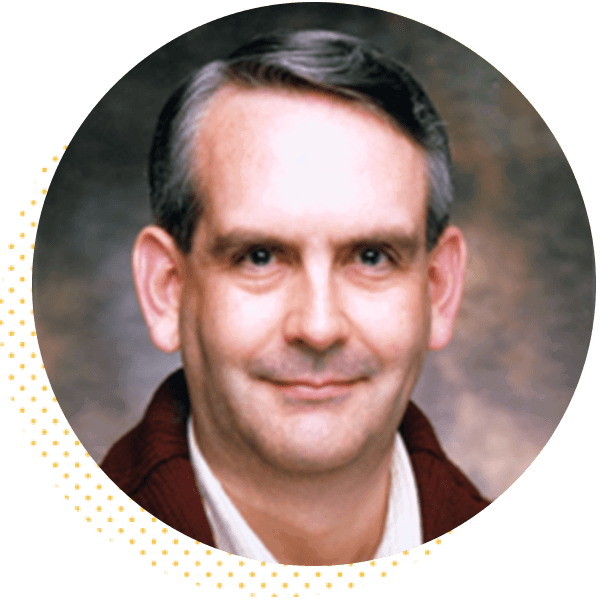 Portrait of a man with short, styled hair and a slight smile, wearing a maroon sweater over a white shirt, set against a softly blurred background. Ideal for professional profiles or biography sections.