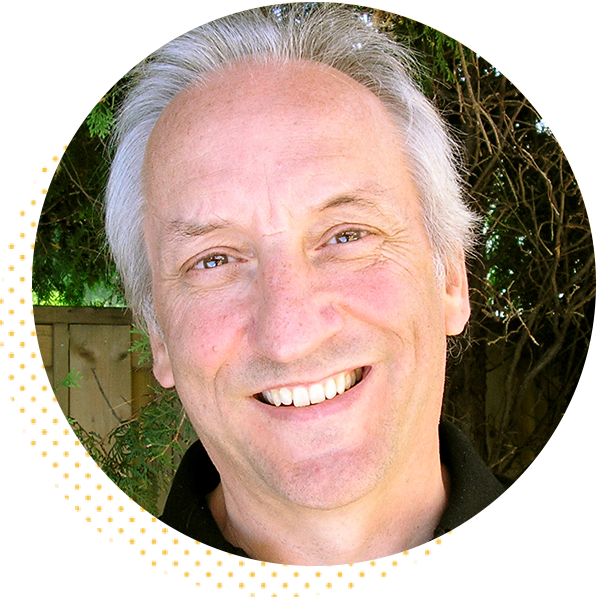 Smiling middle-aged man with gray hair, wearing a black shirt, against a natural background of greenery. Ideal for profiles or articles related to personal development or coaching.