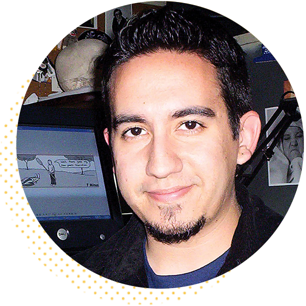 Portrait of a smiling man with dark hair and a goatee, standing in front of a computer monitor displaying a cartoon. The background includes various artistic elements, suggesting a creative workspace.