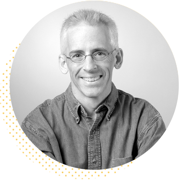 Smiling man with glasses and short gray hair, wearing a collared shirt, against a light background. Ideal for showcasing expertise or professionalism in a personal or corporate context.
