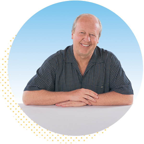 Smiling middle-aged man in a checkered shirt resting his arms on a table against a blue gradient background.