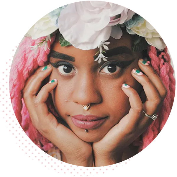 Portrait of a young woman with pink dreadlocks adorned with flowers, showcasing bold makeup and unique piercings, expressing a thoughtful and artistic vibe.