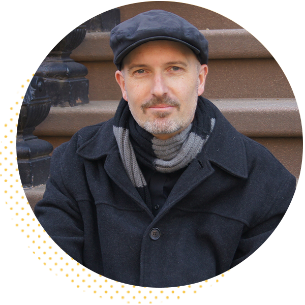 Portrait of a man wearing a black coat, gray scarf, and a flat cap, sitting on steps with a warm expression, showcasing a stylish urban look.