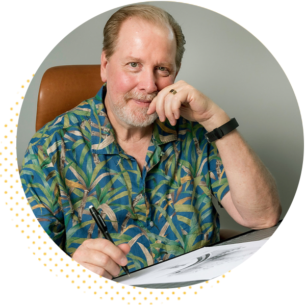 Portrait of a smiling man with a beard, wearing a colorful tropical shirt, seated at a desk with a pen in hand, engaged in drawing or writing. The background features a simple gray wall, complementing the casual and creative atmosphere.