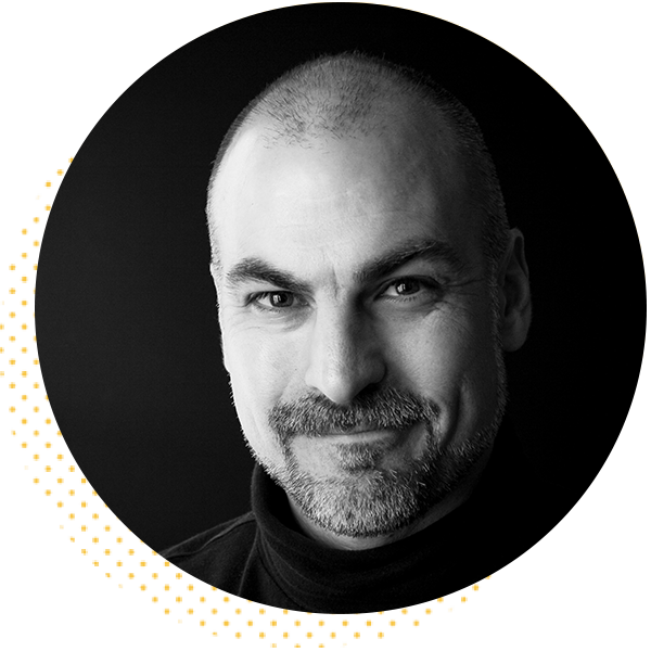 Portrait of a smiling man with a beard, wearing a black turtleneck, set against a dark background. The image features a circular crop with a subtle dotted border, emphasizing the subject's friendly expression and professional demeanor.