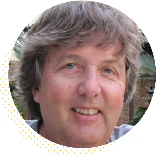 Smiling man with wavy hair in a circular frame, outdoors in a natural setting.