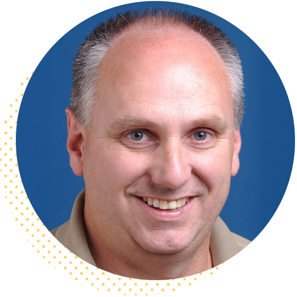 Smiling man with short gray hair and light blue eyes, wearing a beige shirt, set against a blue background. Ideal for professional profiles or team introductions.