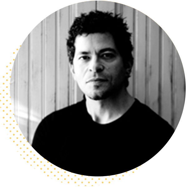 Portrait of a man with short, curly hair, wearing a black shirt, set against a light wooden background. The image is circular and features a minimalist style.