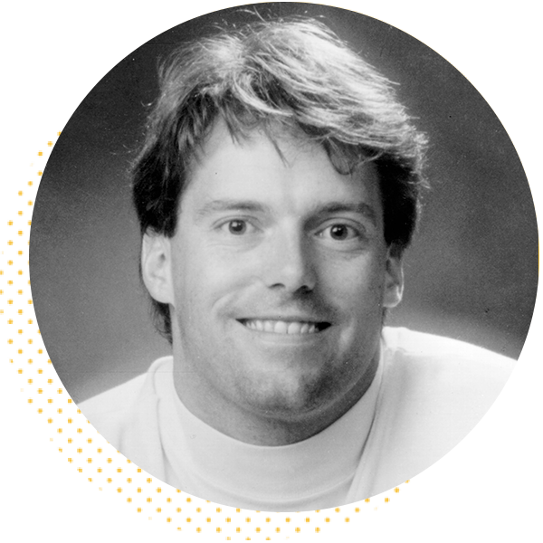 Black and white portrait of a smiling man with medium-length hair, wearing a white turtleneck. The image features a circular crop, highlighting his friendly expression and approachable demeanor.