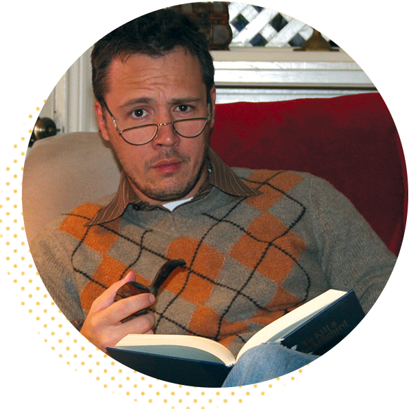 Man reading a book while holding a pipe, wearing glasses and a sweater with an orange and gray pattern, sitting on a couch. The expression conveys curiosity or contemplation, creating a cozy, intellectual atmosphere.