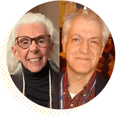 Portrait of two individuals, one with white hair and glasses smiling, wearing a black outfit and pearls, and the other with gray hair, wearing a plaid shirt and a blazer, both looking at the camera in a friendly manner.