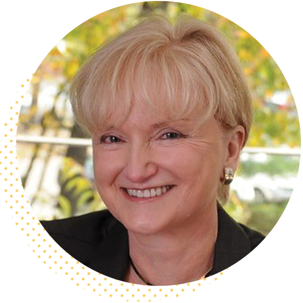 Smiling professional woman with short blonde hair, wearing a black blazer and earrings, set against a blurred background of greenery. Ideal for representing business leadership or expertise.